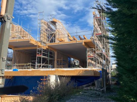 Construcción de un edificio con andamios y cielorrasos de madera bajo un cielo nublado.